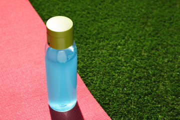 Bottle of light blue drink and mat on green grass, space for text
