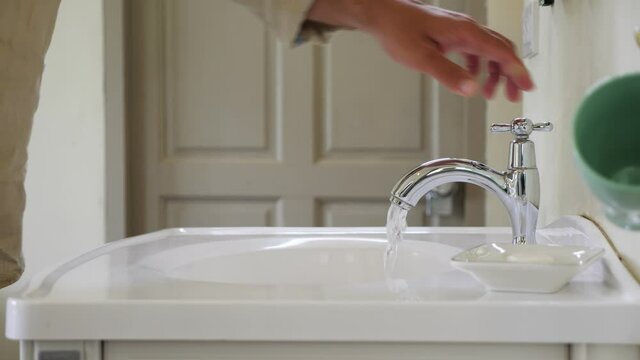 Strong flow from faucet to sink, man put arm on valve, turn off water. Close shot of bathroom equipment, only male hand and sink is visible. Guy complete bathing routines and stop running water