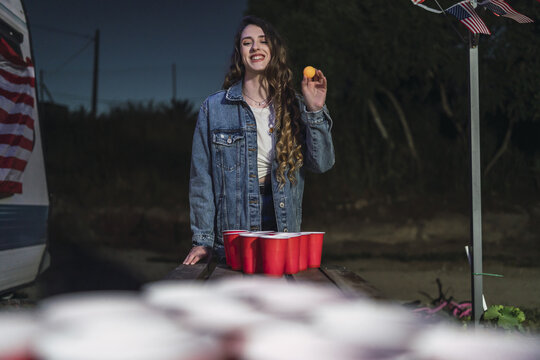 Young Spanish female getting ready to throw the ball in beer pong cups next to US flags