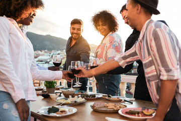 Happy multiracial friends having dinner and cheering with wine outdoor at home - Main focus on...