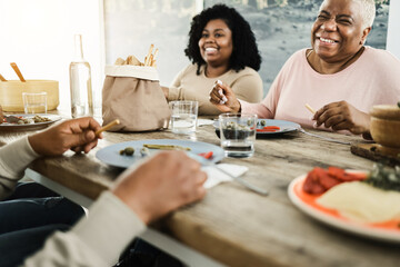 Happy black family eating lunch at home - Father, daughter, son and mother having fun together sitting at dinner table - Main focus on mum face