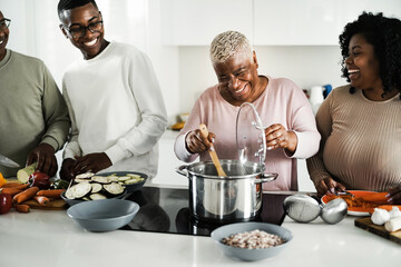 Happy black family cooking vegan food inside kitchen at home - Focus on mother face