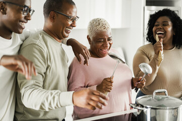 Happy black family dancing while cooking vegan food inside kitchen at home - Focus on mother face