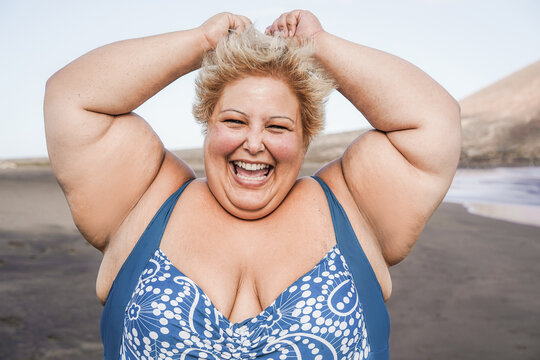 Curvy woman smiling on camera wearing bikini with beach in background - Focus on face