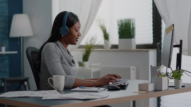 African american student putting headphones listening fun music typing school ideas on internet using elearning platform on computer. Black woman working remote from home enjoying fun break
