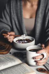 A young girl drinks morning coffee, eats a healthy breakfast and reads a book. Morning routine. Stylish manicure. Correct habits. Holding a cup in his hands