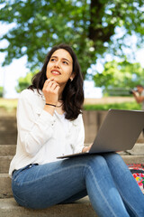 Young businesswoman sitting on steps outdoors and working on laptop. Beautiful girl learning in the park