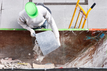 bricklayer worker in motion blur in construction site depositing rubble in container for pickup by...