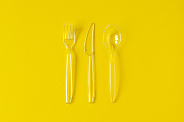Transparent plastic fork, knife, spoon on yellow background. Minimalist disposable tableware....