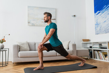 sportive man practicing crescent lunge pose on yoga mat at home - Powered by Adobe