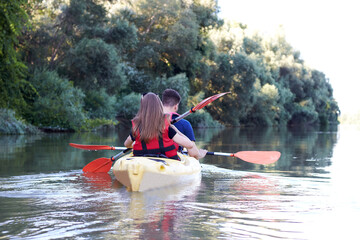 Couple (man and woman) paddle a yellow kayak near trees at Danube river at summer