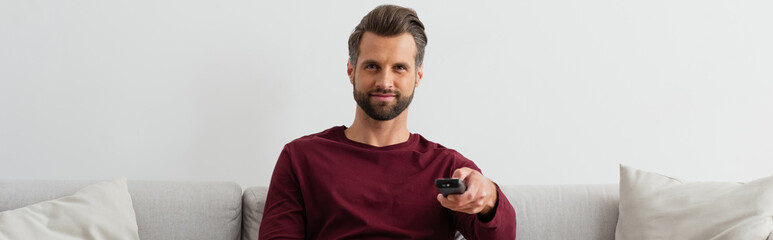 positive man clicking channels while watching tv at home, banner