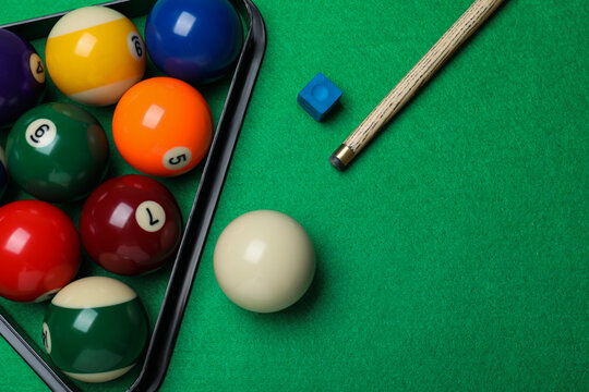 Set of billiard balls with rack, cue and chalk on green table, flat lay. Space for text