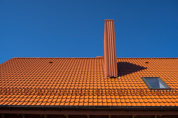 Fototapeta premium Red corrugated metal profile roof installed on a modern house. The roof of corrugated sheet. Roofing of metal profile wavy shape. Modern roof made of metal. Metal roofing.