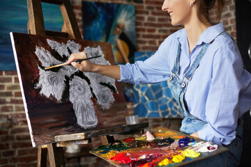 Young beautiful female artist painting still life with sunflower on canvas using oil paintings and art brush. Painter creating artwork in art studio. Relaxation, leisure, hobby, stress management.