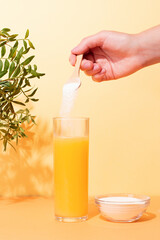 Woman adding collagen powder to orange juice on colorful background