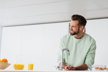 happy man washing cherry tomatoes while preparing breakfast in kitchen