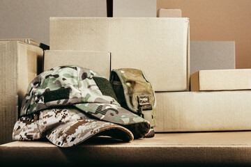 Photo of various military camouflaged caps with pouch laying on stacked cardboard boxes.