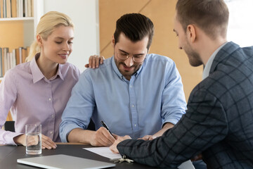Happy millennial couple signing contract, excited family making insurance or investment deal at meeting with manager, satisfied clients purchasing first own apartment, putting signature on document