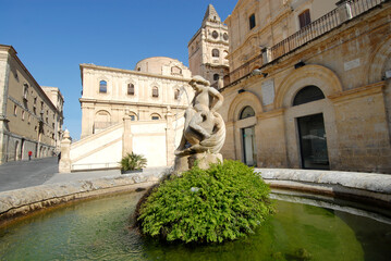 Fototapeta premium round fountain of Noto with little angel and in the background the baroque church with large staircase of San Francesco d'Assisi all'Immacolata. 