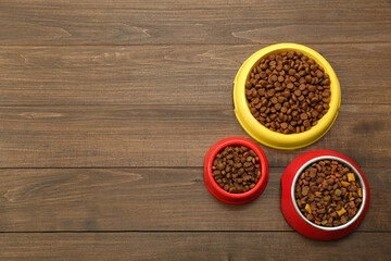 Dry food in pet bowls on wooden background, flat lay. Space for text