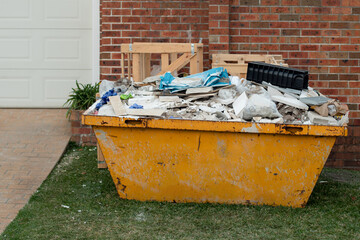 Skip bin full of household waste rubbish on the front yard. House clean up and renovation concept. - obrazy, fototapety, plakaty