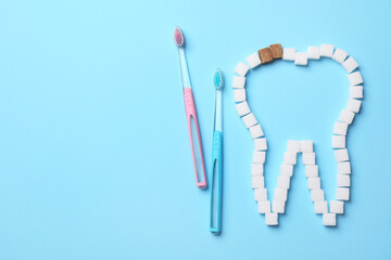 Composition with tooth outline made of sugar cubes near toothbrushes, flat lay. Caries problem