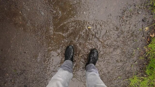 Person springt in schmutzige Pf&uuml;tze und das Wasser spritzt. Zeitlupe