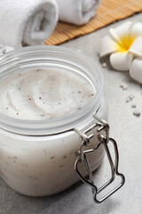 Body scrub, towels and plumeria flowers on grey table, closeup