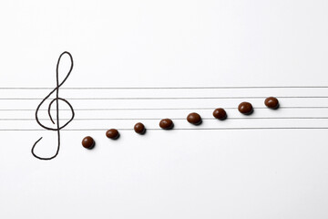 Music staff with treble clef and chocolate candies as notes on white paper, flat lay. Creativity...