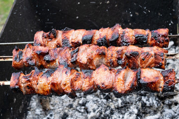The fried shish kebab cooking on a metal spit. Fried meat is made in a barbecue. On charcoal. Street food