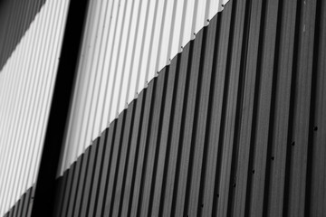 Fototapeta premium Details of black and white corrugated iron sheet used as a facade of a warehouse or factory. Texture of a seamless corrugated zinc sheet metal aluminum facade. Architecture. Metal texture.