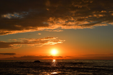 Sunset over the sea bay, which colors the sky and picturesque clouds from red to blue-emerald colors, leaving a golden trace on the sea.