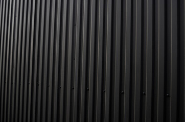 Obraz premium Black corrugated iron sheet used as a facade of a warehouse or factory. Texture of a seamless corrugated zinc sheet metal aluminum facade. Architecture. Metal texture.
