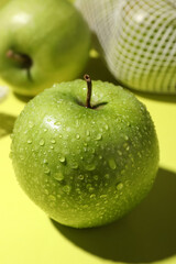 Ripe apple with water drops on light green background, closeup