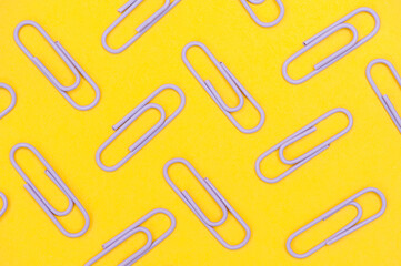 Purple paper clips on yellow background. flat lay