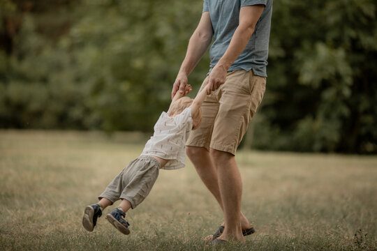 young Father with his son playing in the park in the summer. daddy circles the little boy by the arms. Family leisure concept, outdoor play, parenting. Father's day. Selective focus.