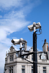 Close-up of CCTV cameras against a building and blue sky.