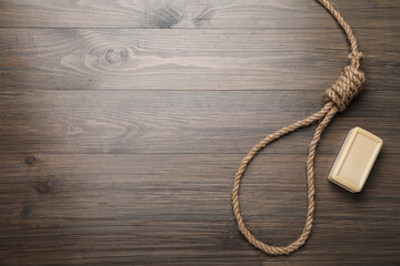 Rope noose and soap bar on wooden table, flat lay. Space for text