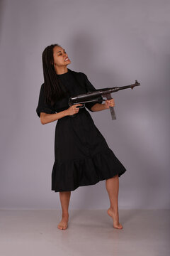 Curly woman in black dress with vintage submachine gun on grey background