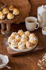 Homemade profiteroles with powdered sugar. Side view, wooden background.