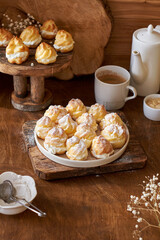 Homemade profiteroles with powdered sugar. Side view, wooden background.