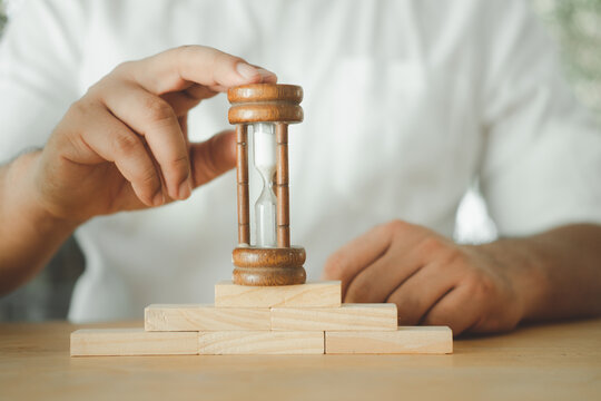 Businessman in white shirt holds an hourglass on wooden block.