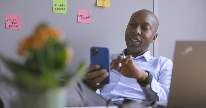 Smiling businessman sitting at desk in office, using smartphone