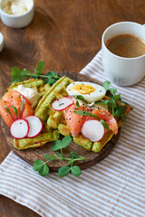 Spinach waffles with salmon, egg and radish. Side view, wooden background.