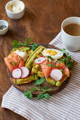 Spinach waffles with salmon, egg and radish. Side view, wooden background.
