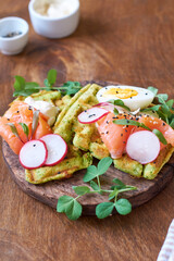 Spinach waffles with salmon, egg and radish. Side view, wooden background.