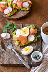 Spinach waffles with salmon, egg and radish. Side view, wooden background.