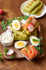 Spinach waffles with salmon, egg and radish. Side view, wooden background.