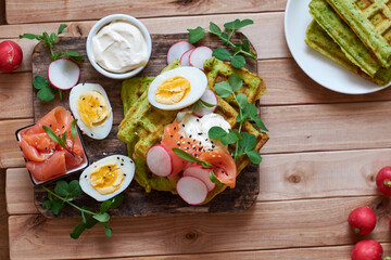 Spinach waffles with salmon, egg and radish. Top view, wooden background.